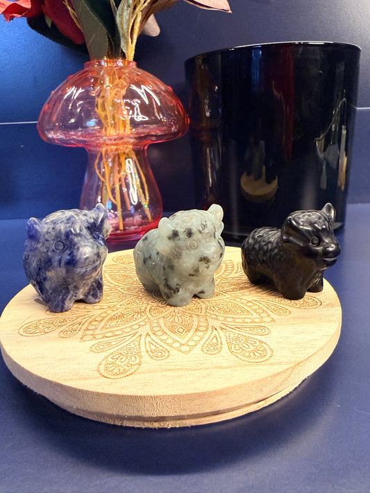 Three crystal cows sitting on a decorative wooden coaster in front of a glass mushroom and black jar