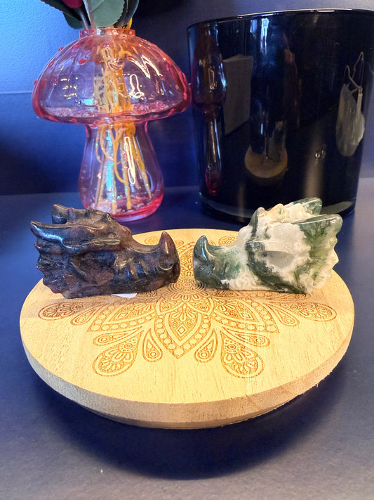 Two crystal dragon heads sitting on a decorative wooden coaster in front of a glass mushroom and black jar