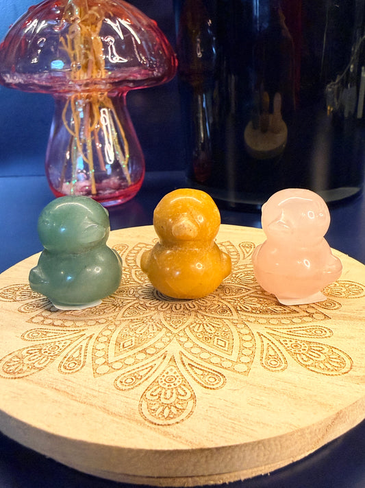 Three crystal ducks sitting on a decorative wooden coaster in front of a glass mushroom and black jar