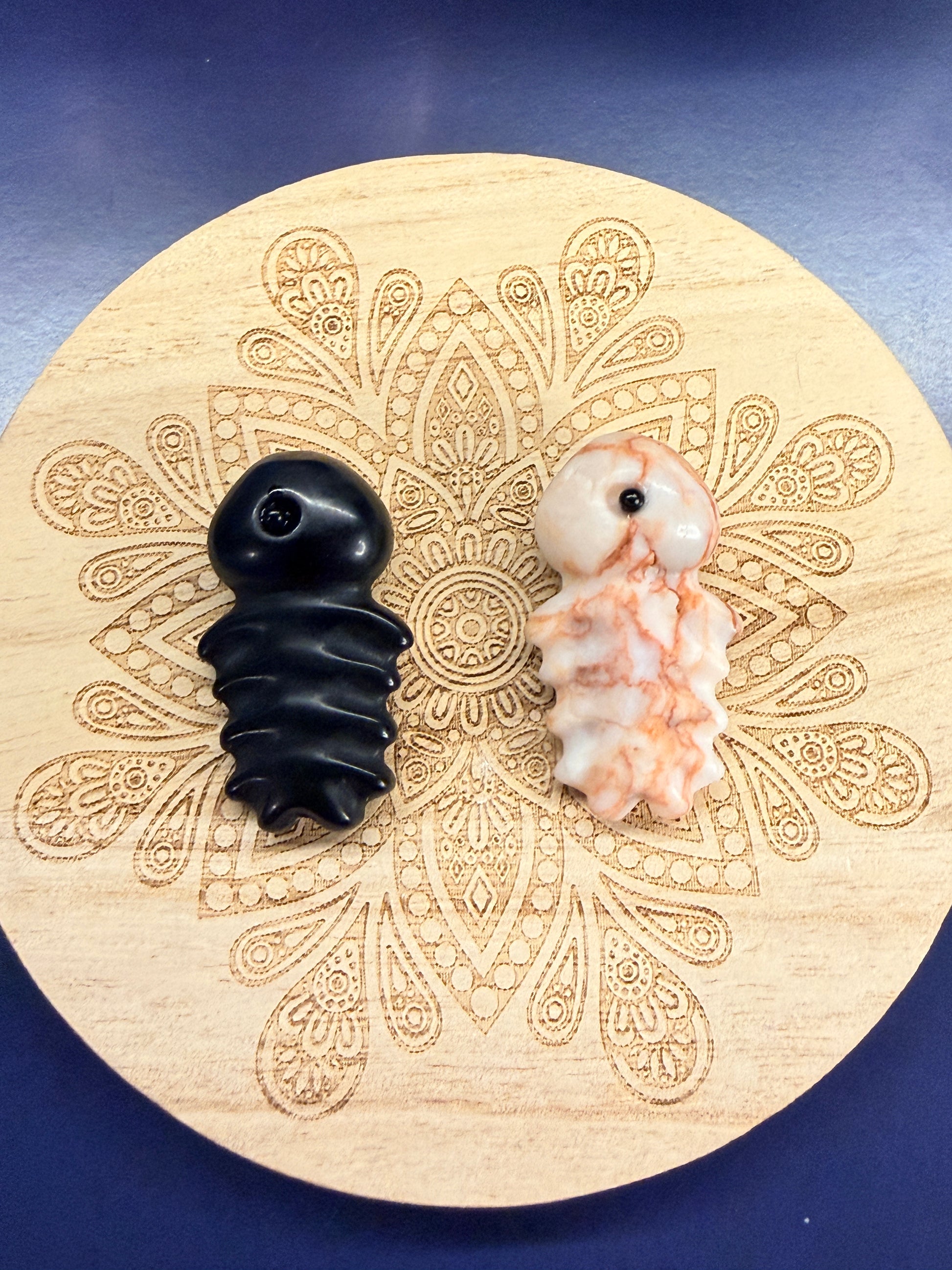Two fish bone crystals, obsidian and red jasper, sitting on a decorative wooden coaster 