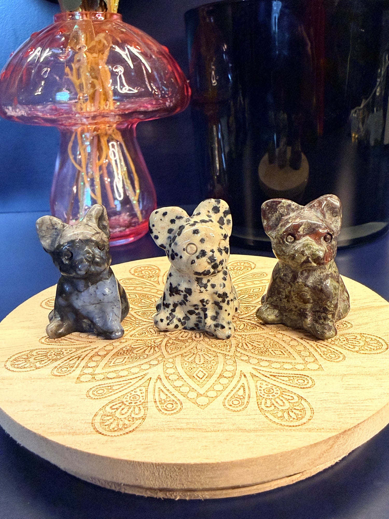 Three crystal bulldogs sitting on a decorative wooden coaster in front of a glass mushroom and black jar