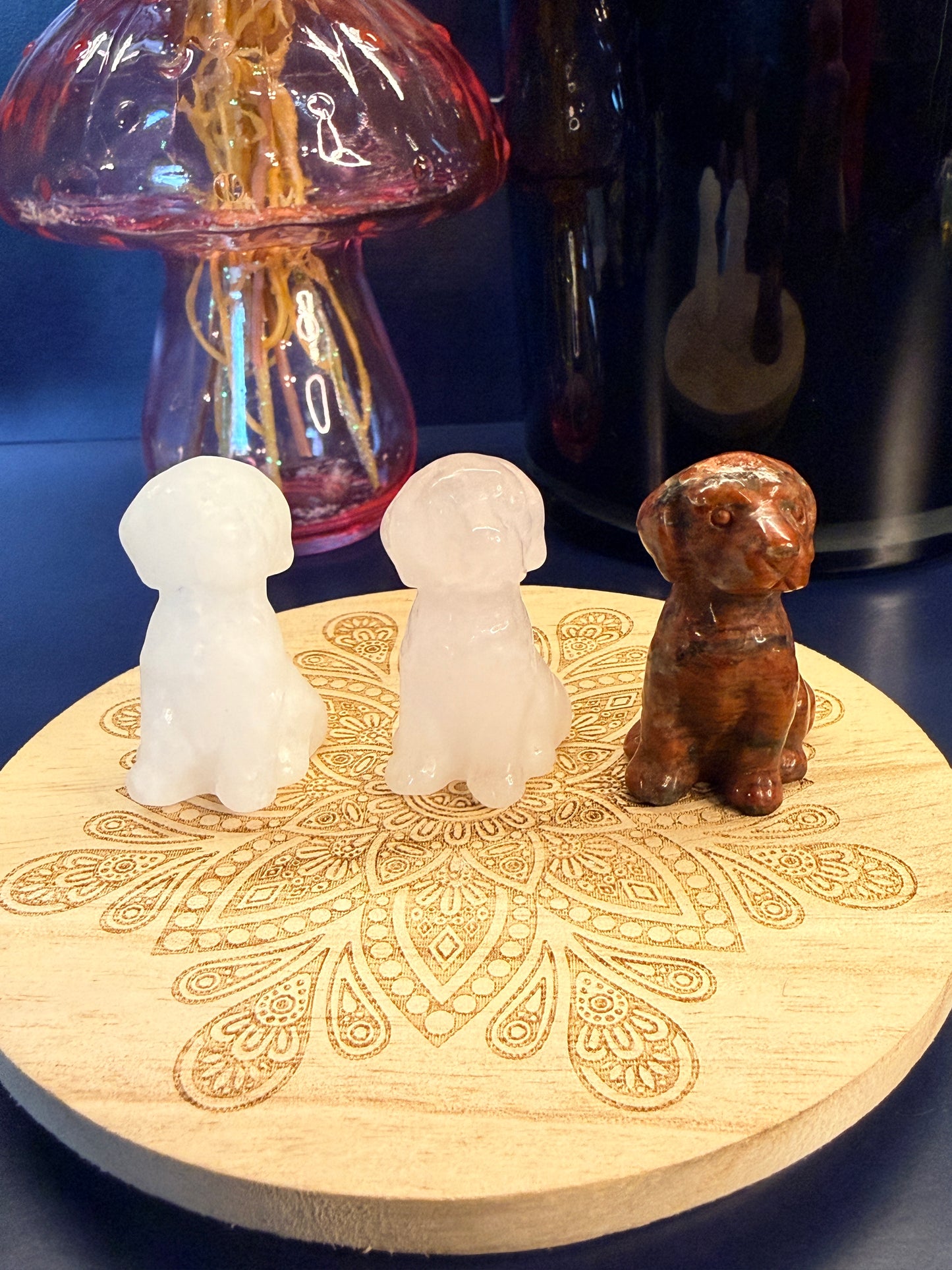 Three crystal Labrador dogs sitting on a decorative wooden coaster in front of a glass mushroom and black jar