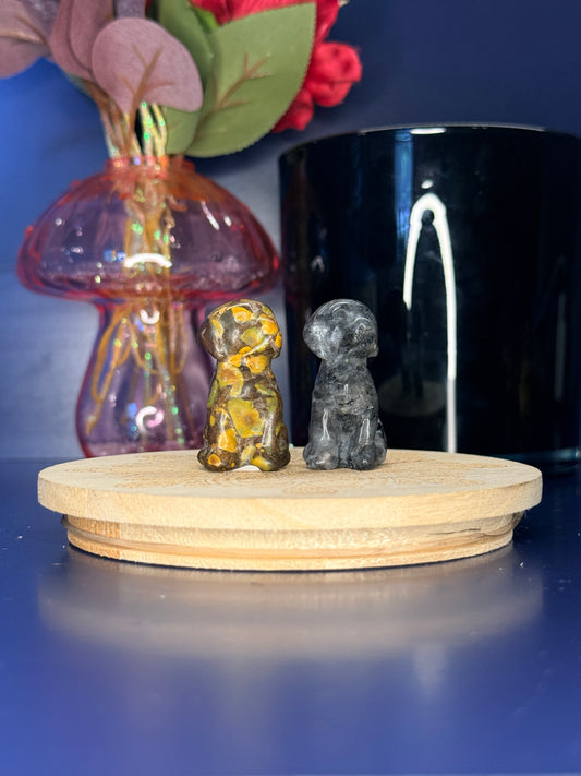 Grey and Yellow crystal dog carvings in front of a pink vase and black jar on a wooden coaster against a blue background
