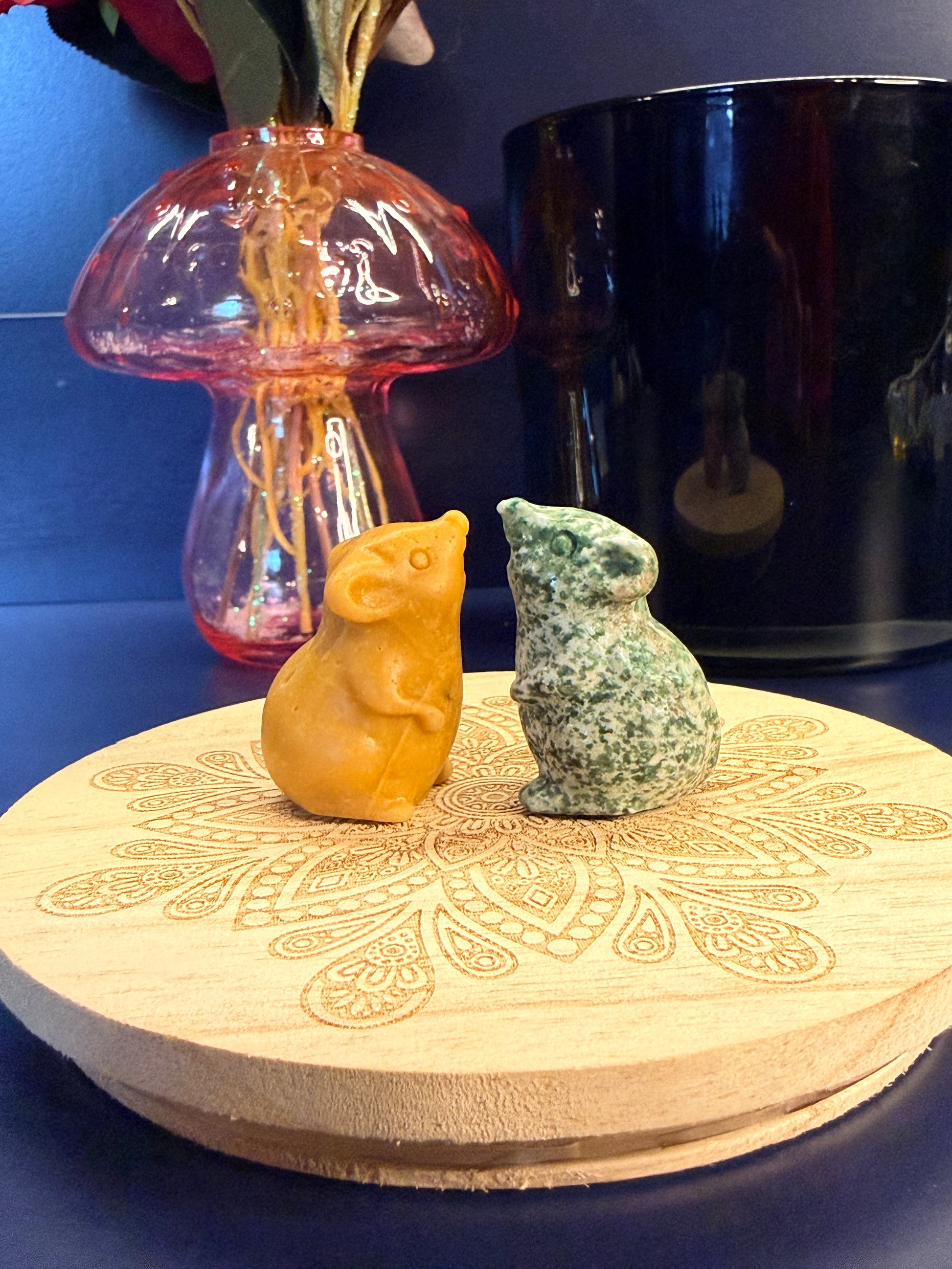 Two crystal mice sitting on a decorative wooden coaster in front of a glass mushroom and black jar
