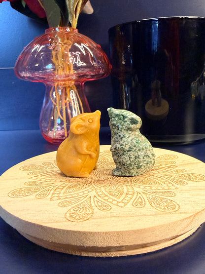Two crystal mice sitting on a decorative wooden coaster in front of a glass mushroom and black jar