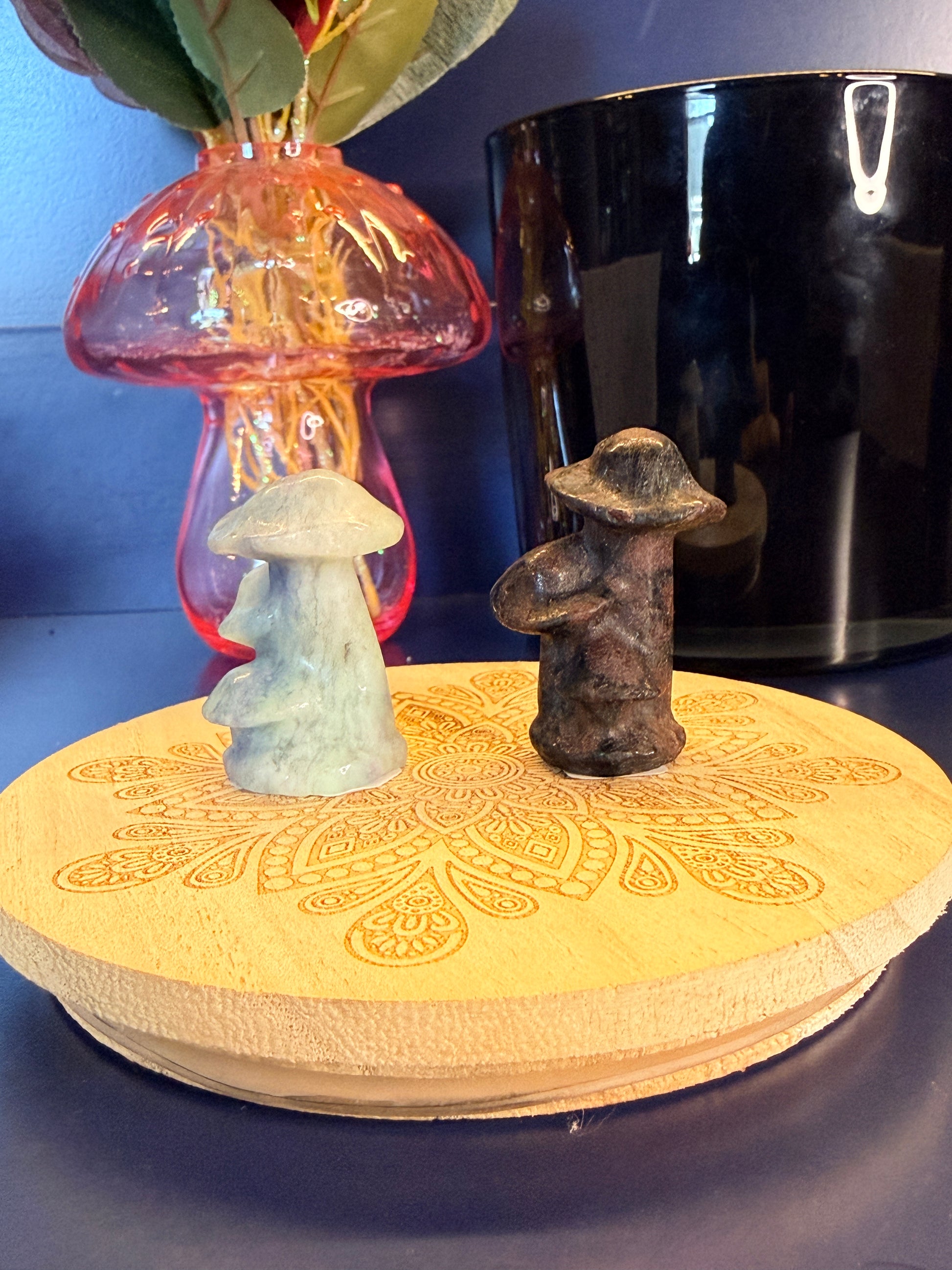 Two crystal mushrooms, blue and dark red, sitting on front of a mushroom vase and black jar