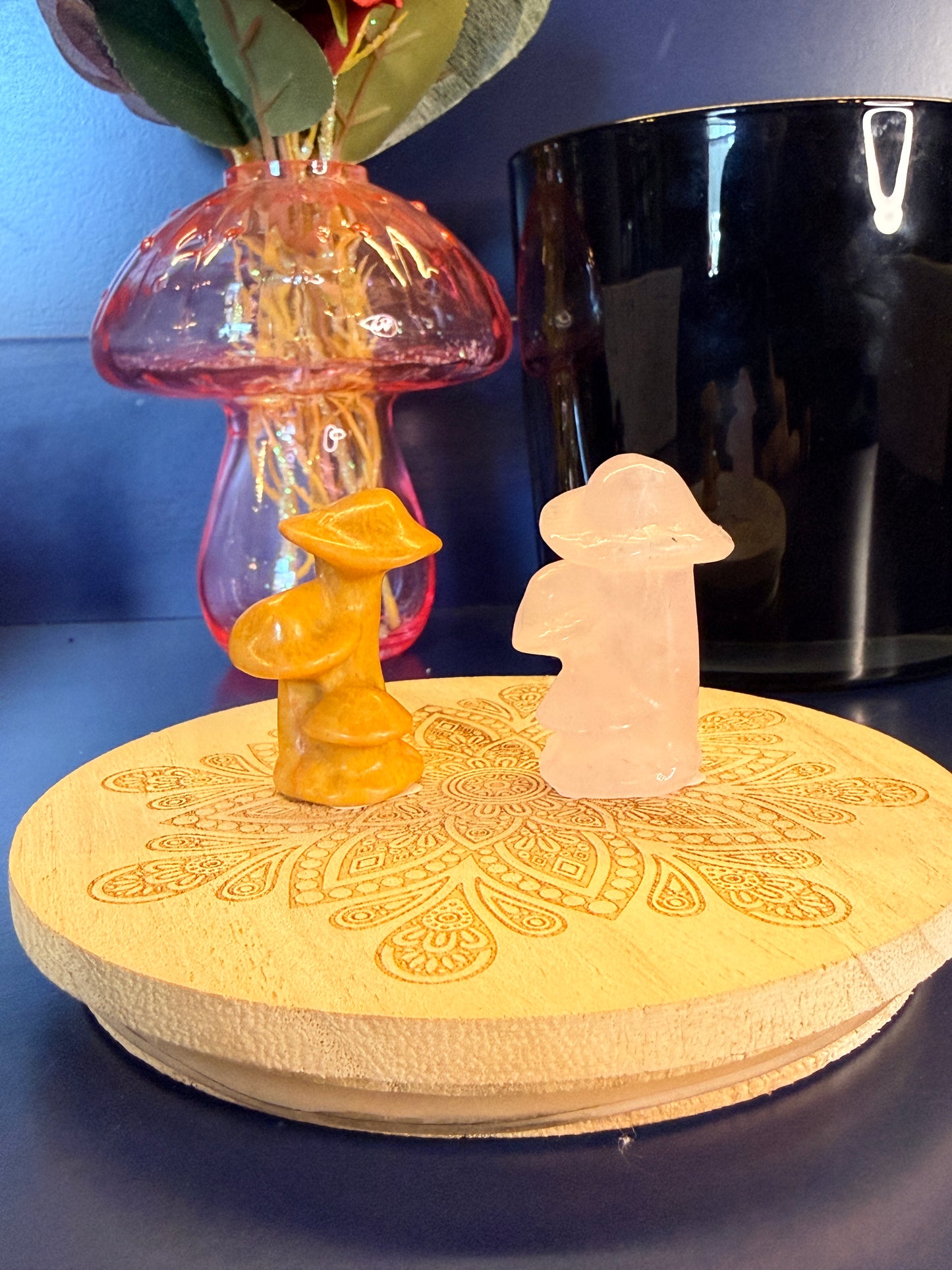 Two crystal mushrooms, orange and pink, sitting on front of a mushroom vase and black jar