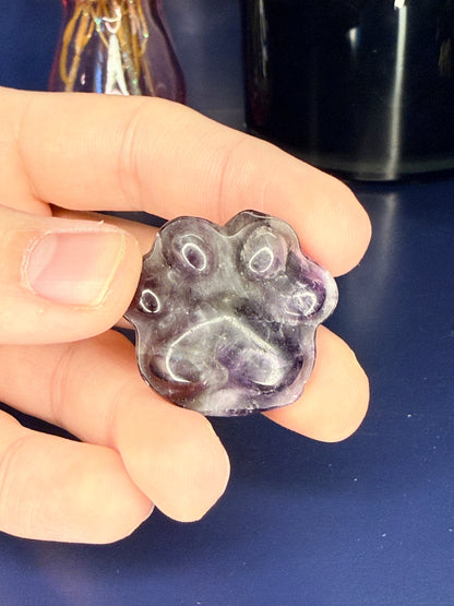purple amethyst paw carving in front of a pink vase and black jar on a wooden coaster against a blue background