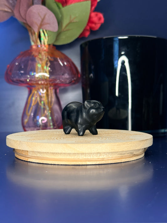 black obsidian elephant carving in front of a pink vase and black jar on a wooden coaster against a blue background