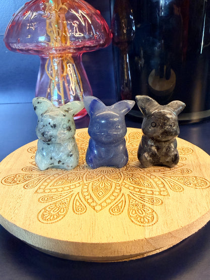 Three pikachu crystals sitting on a decorative wooden coaster in front of a glass mushroom and black jar