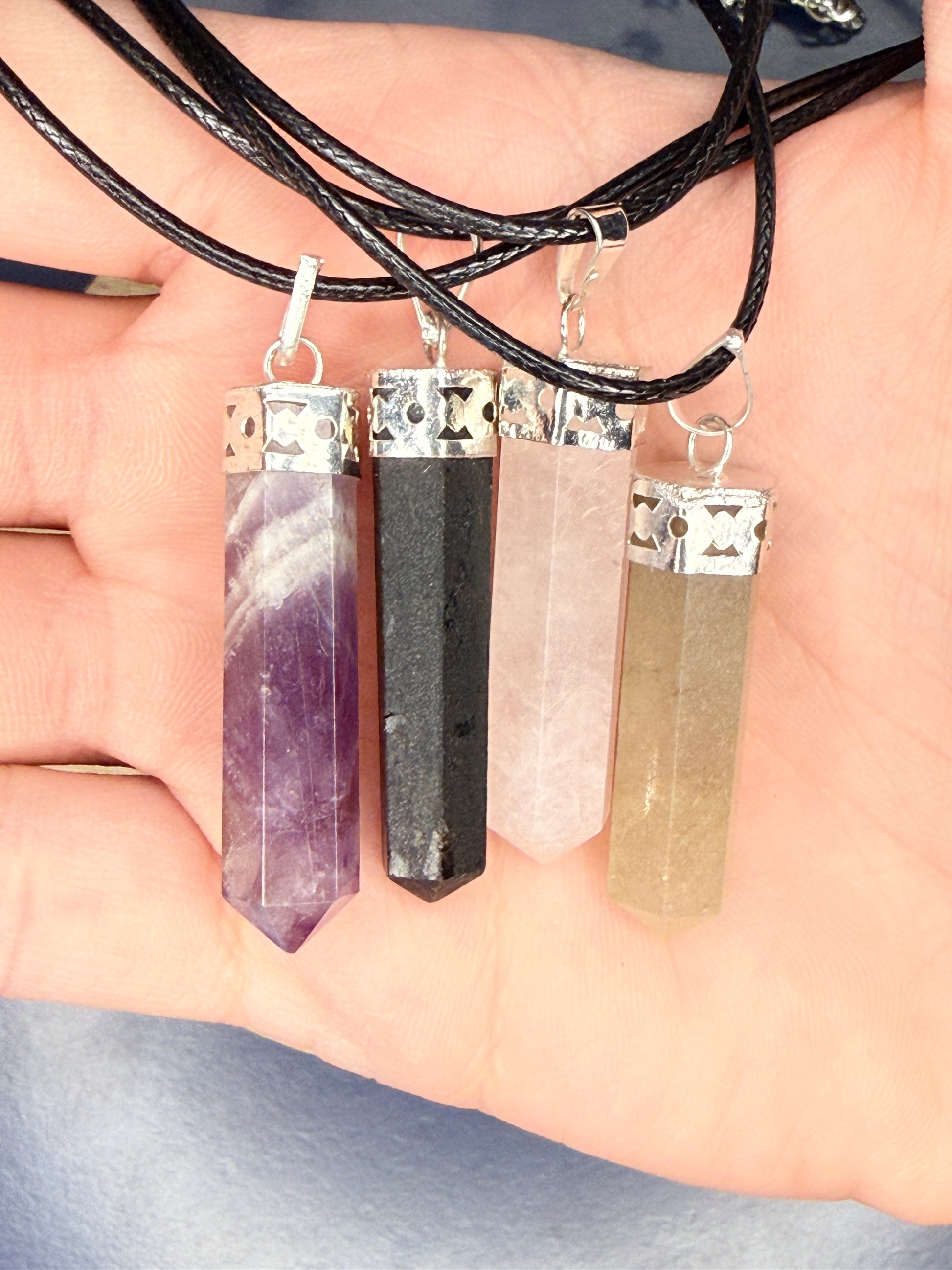 Hand holding four differently colored crystal pendants on nylon chains