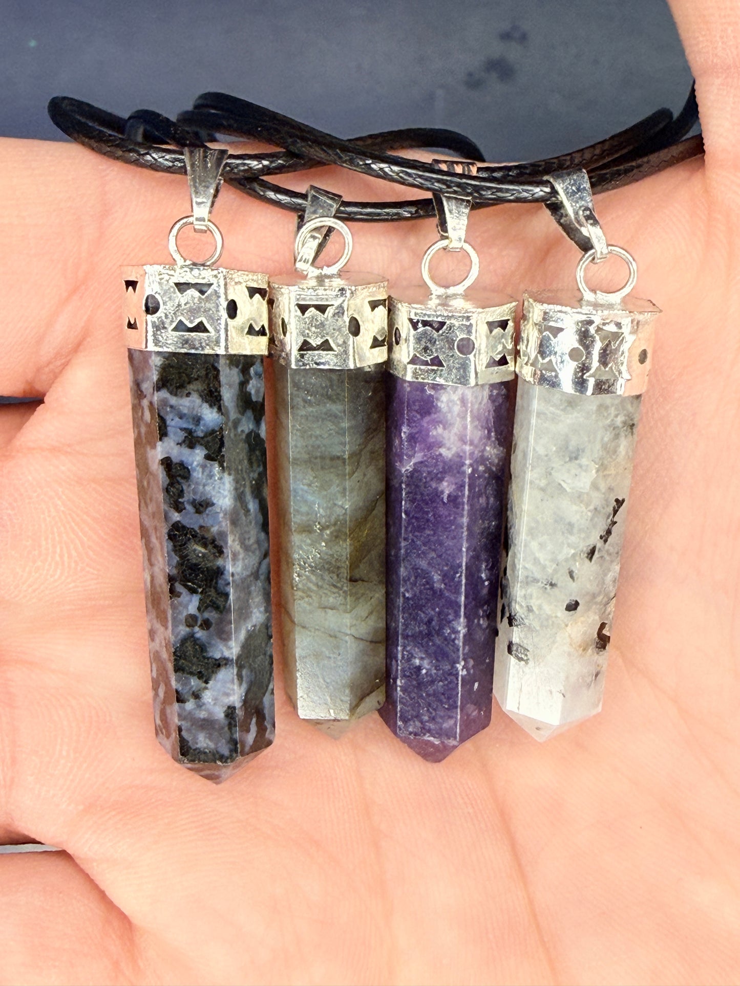 Hand holding four differently colored crystal pendants on nylon chains