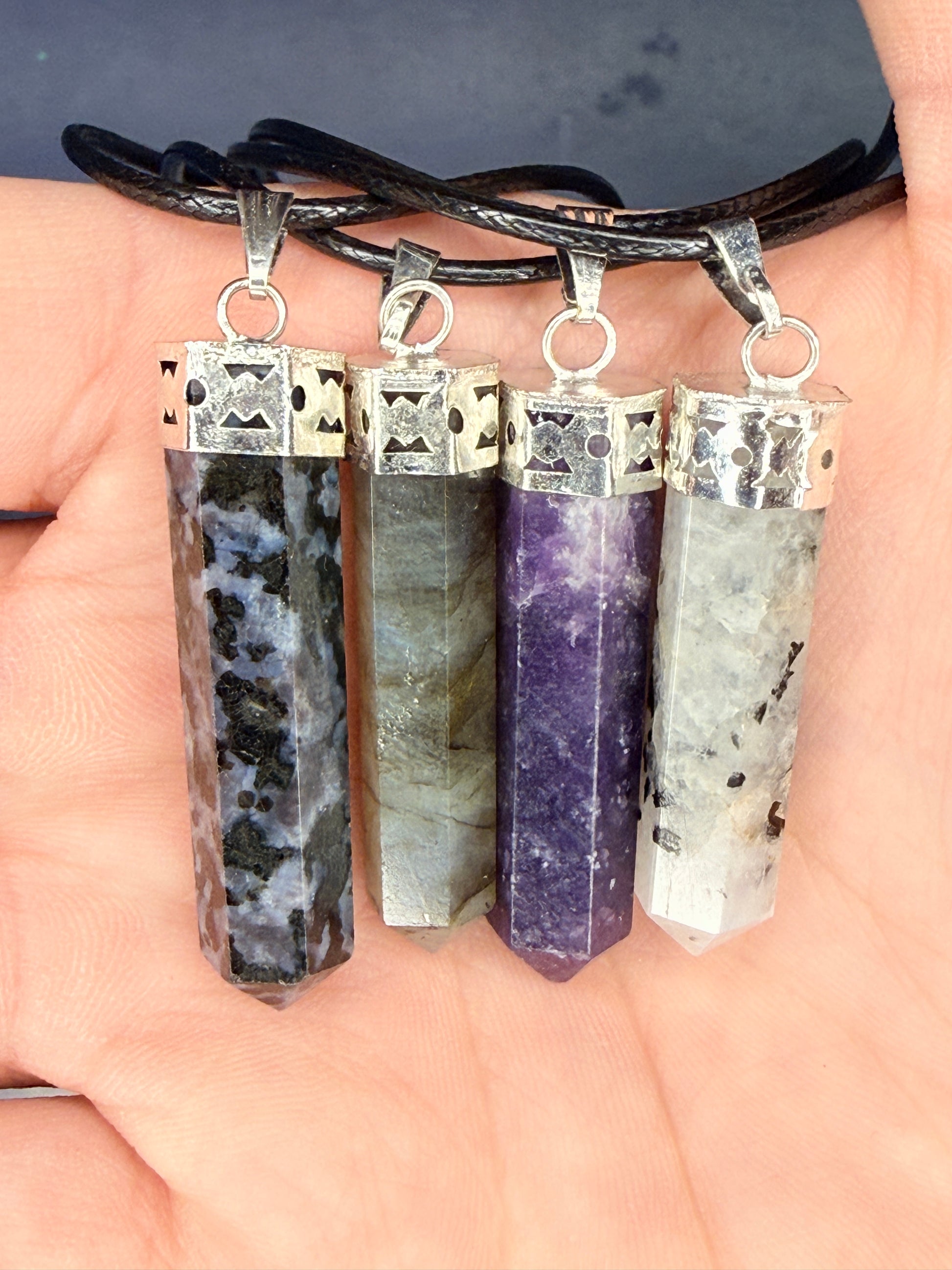 Hand holding four differently colored crystal pendants on nylon chains