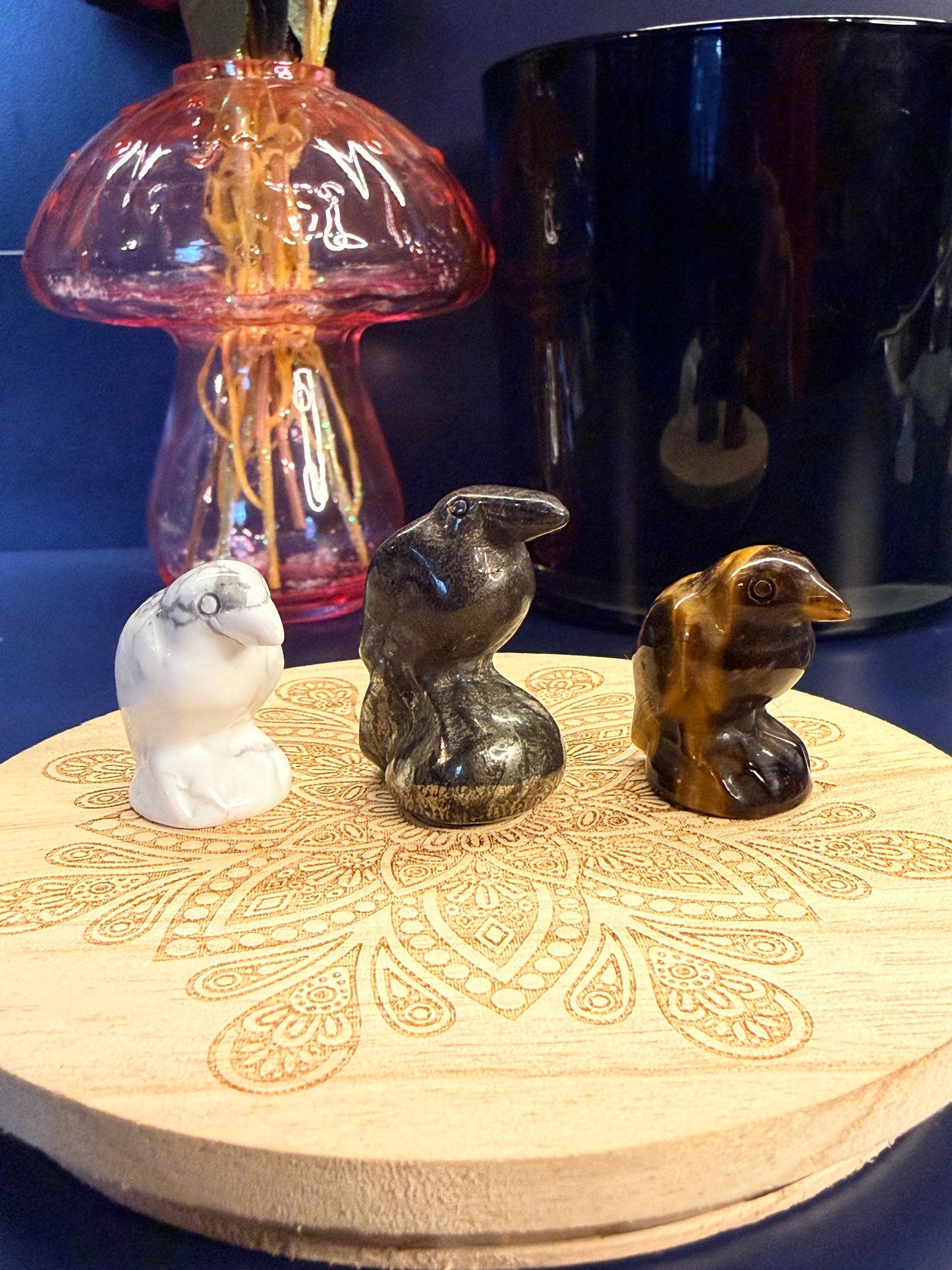Three crystal ravens sitting on a decorative wooden coaster in front of a glass mushroom and black jar