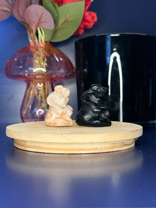 Red and black crystal elephant carvings in front of a pink vase and black jar on a wooden coaster against a blue background