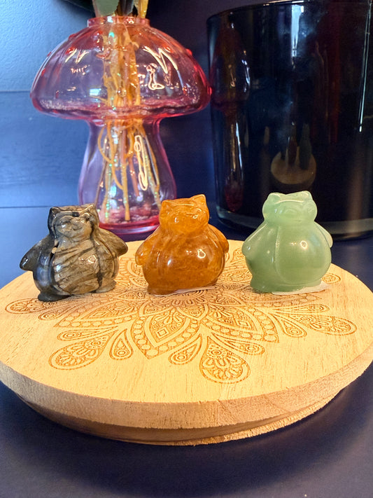 Three different crystal snorlax sitting on a wooden coaster in front of a glass mushroom and black jar