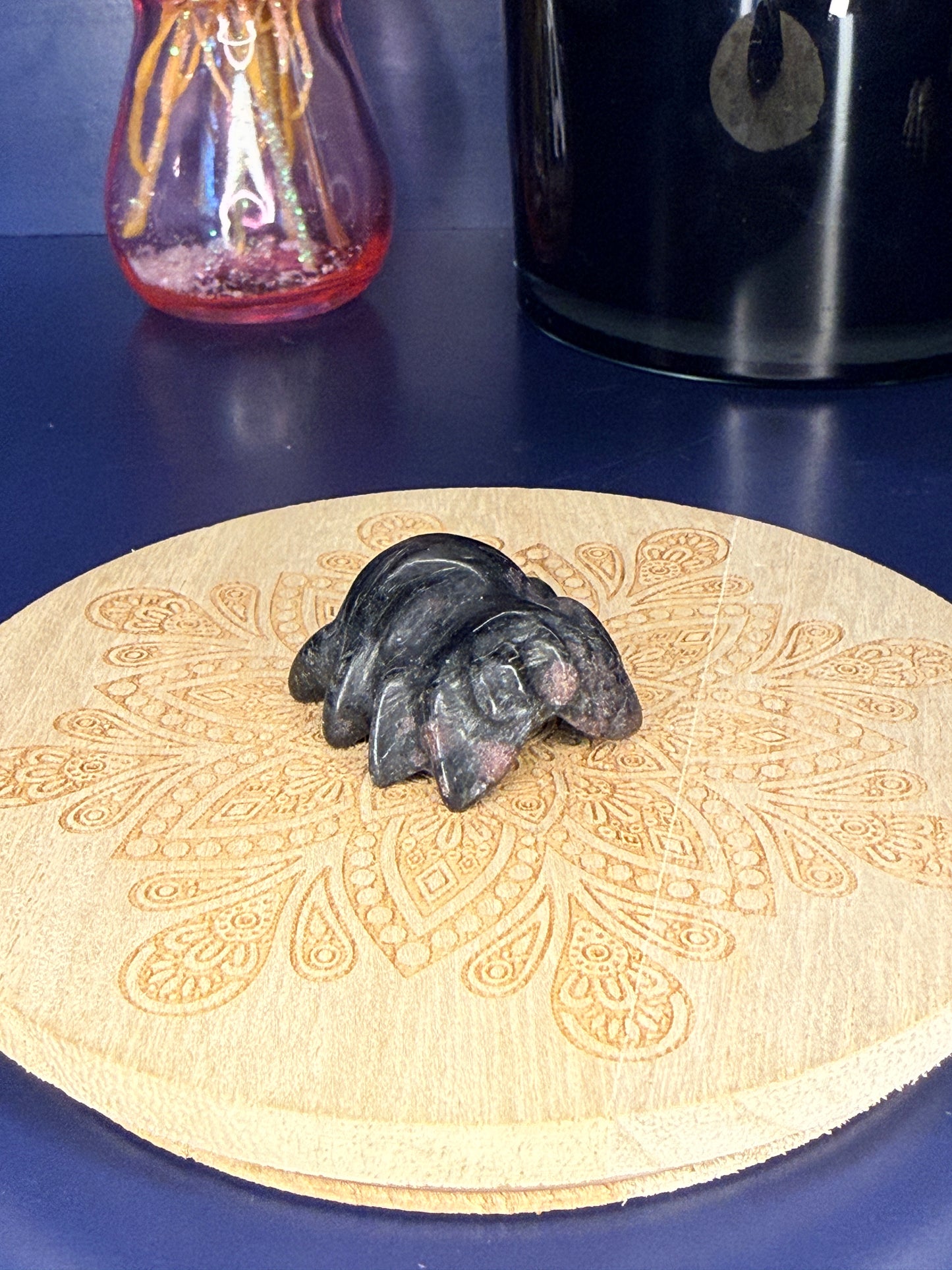 black garnet spider carving in front of a pink vase and black jar on a wooden coaster against a blue background