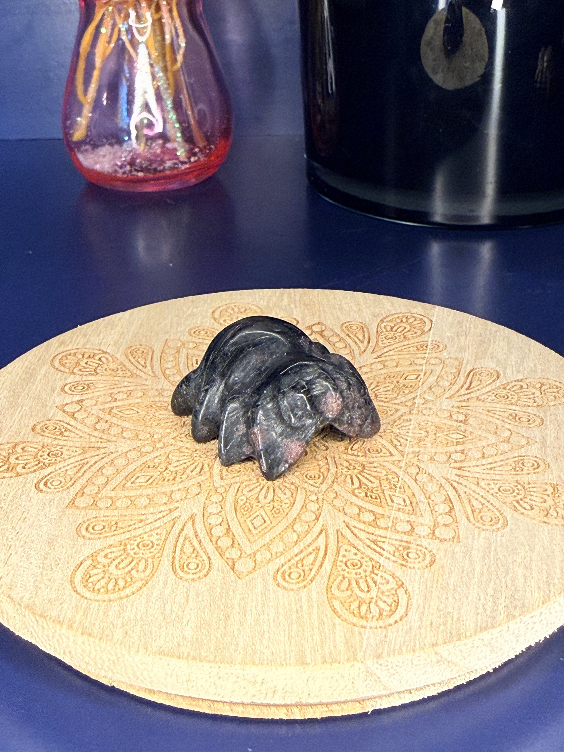 black garnet spider carving in front of a pink vase and black jar on a wooden coaster against a blue background
