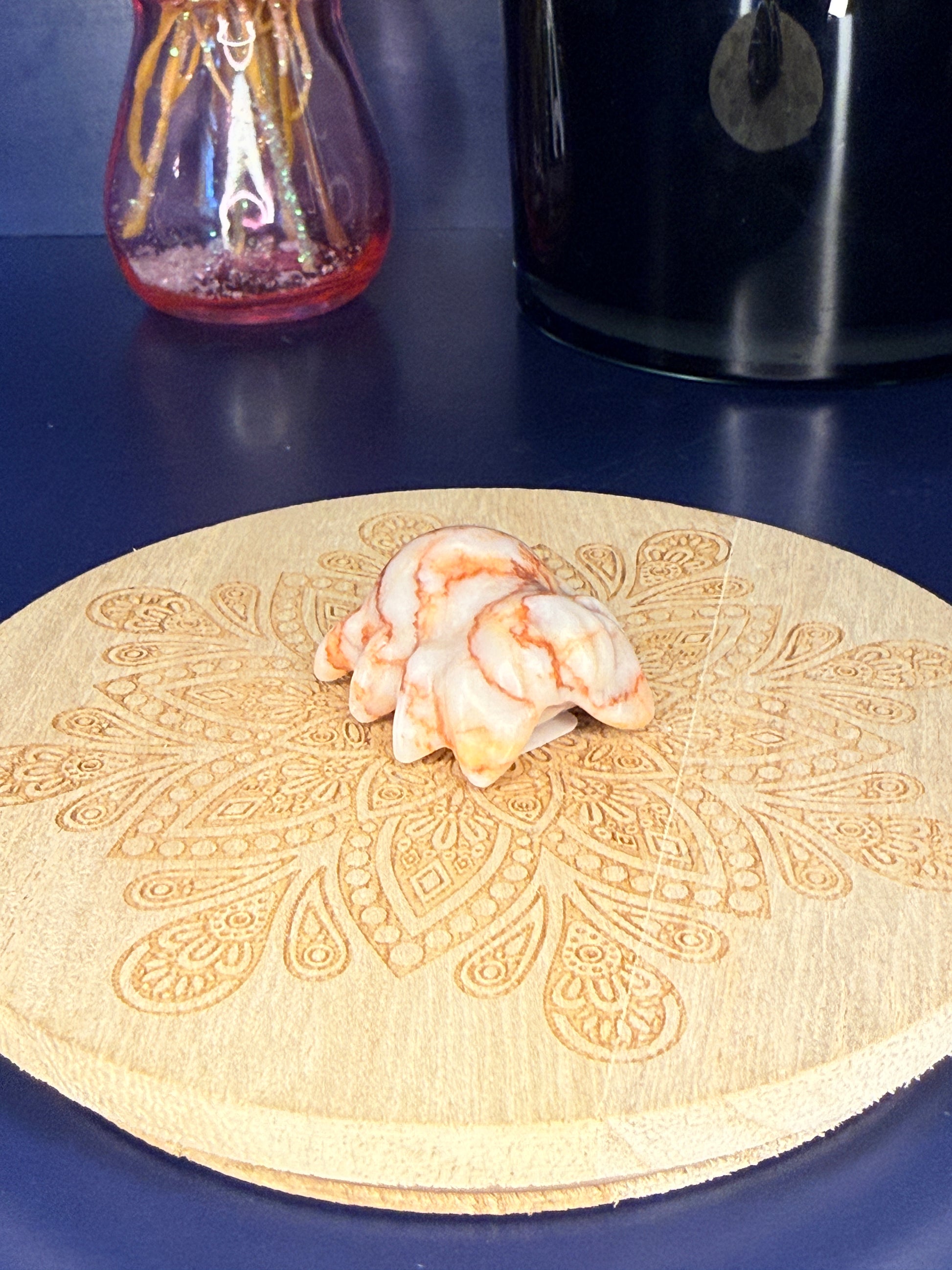 red and white crystal spider carving in front of a pink vase and black jar on a wooden coaster against a blue background