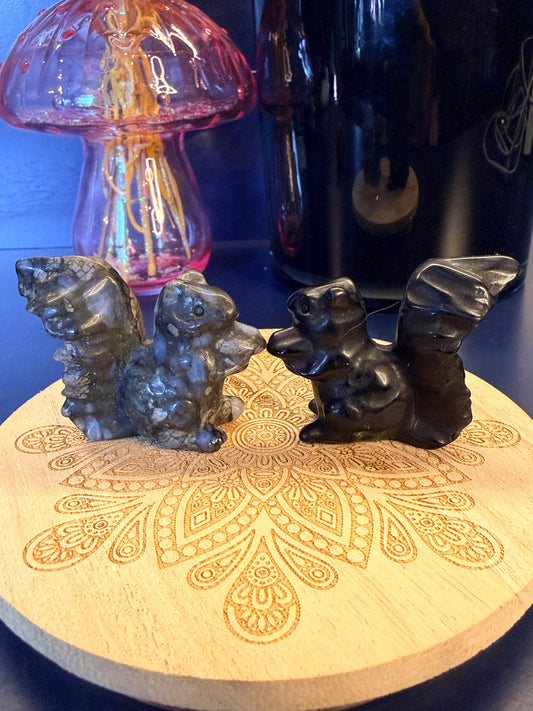Two crystal squirrels sitting on a decorative wooden coaster in front of a glass mushroom and black jar