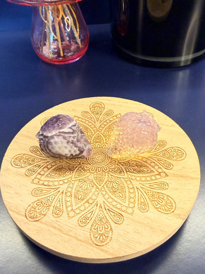 Two strawberry crystals sitting on a decorative wooden coaster in front of a glass mushroom and black jar