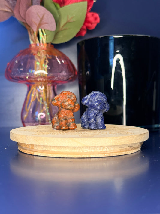 Red and blue crystal dog carvings in front of a pink vase and black jar on a wooden coaster against a blue background