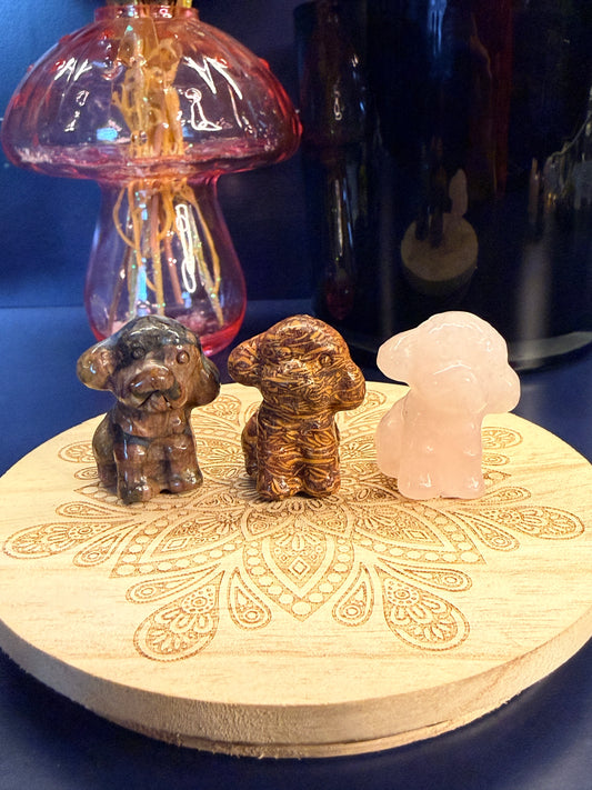Three crystal toy poodles sitting on a decorative wooden coaster in front of a glass mushroom and black jar