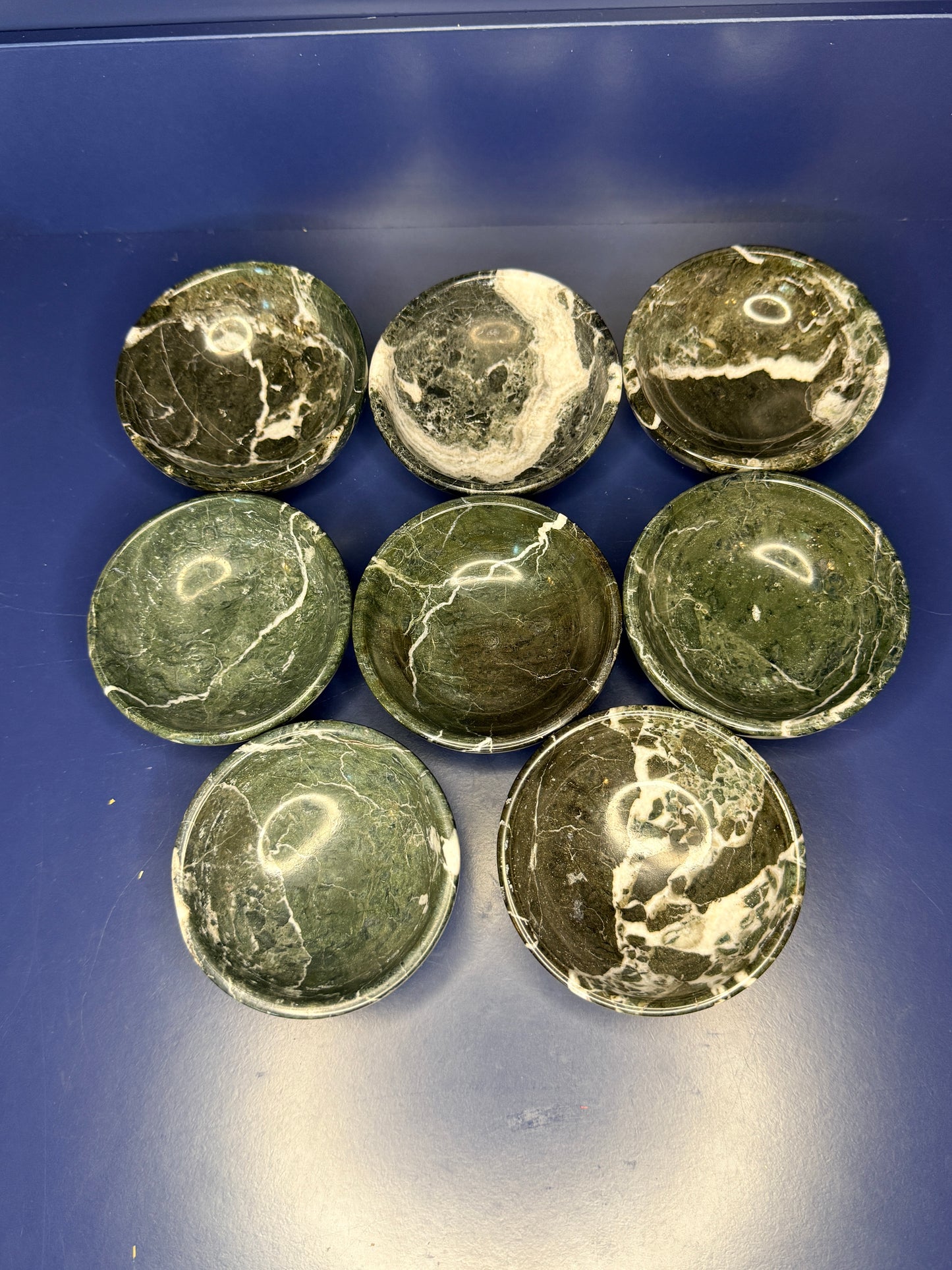 Eight dark green and white green onyx bowls on a blue background