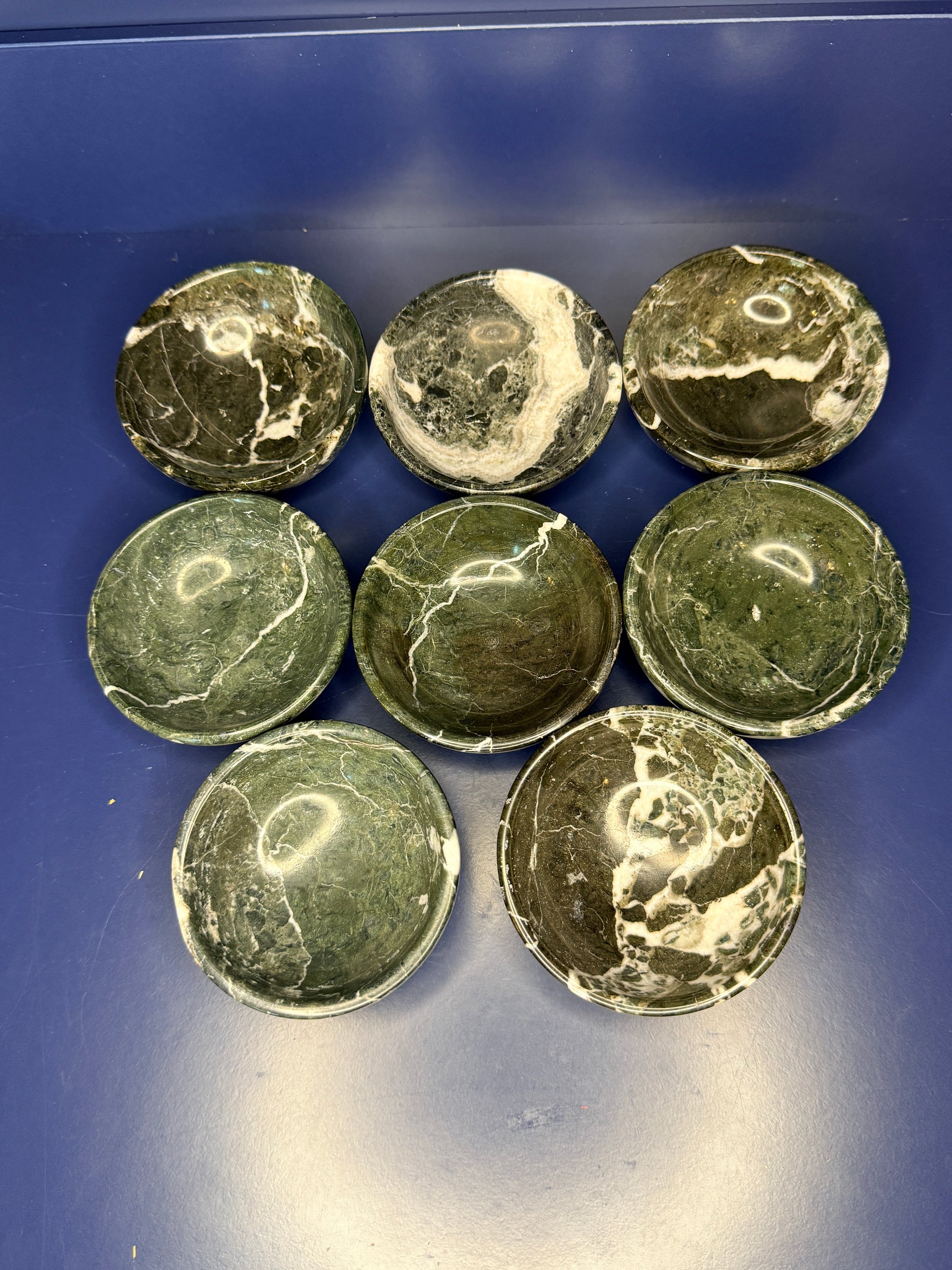 Eight dark green and white green onyx bowls on a blue background