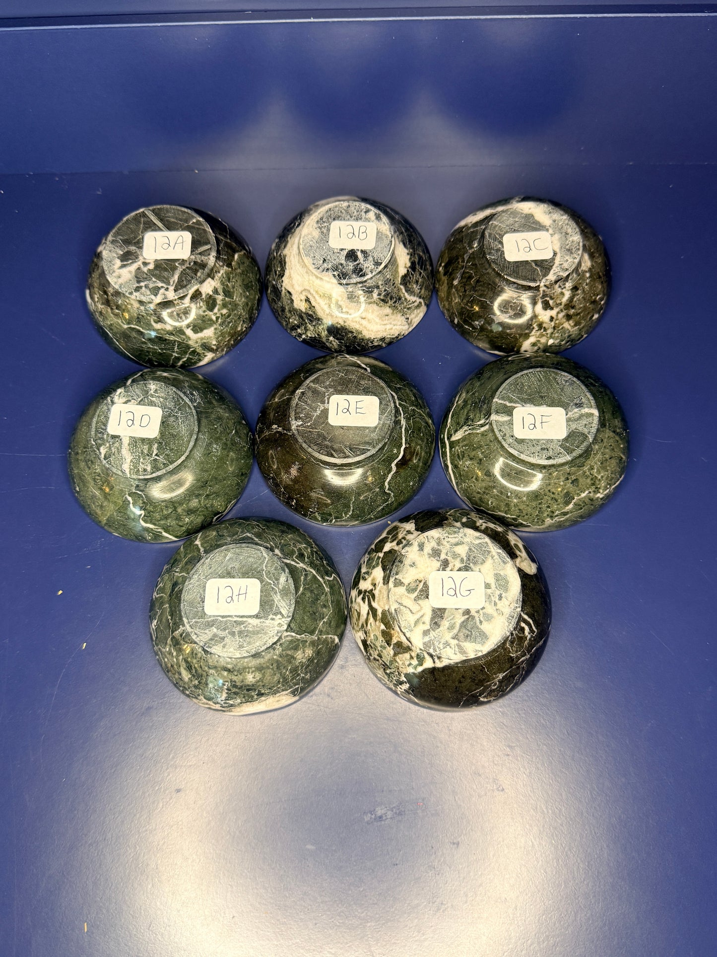 Eight dark green and white green onyx bowls with labels on a blue background