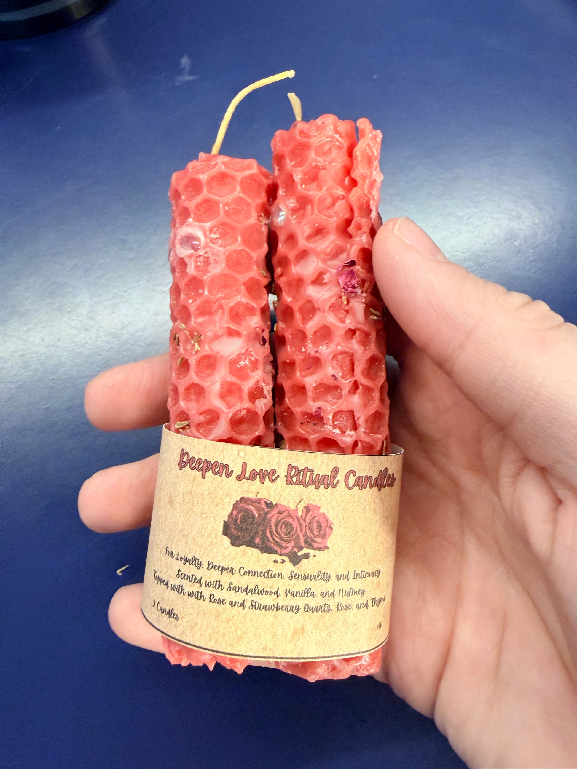 Two red beeswax candles with a label held by a hand against a blue background