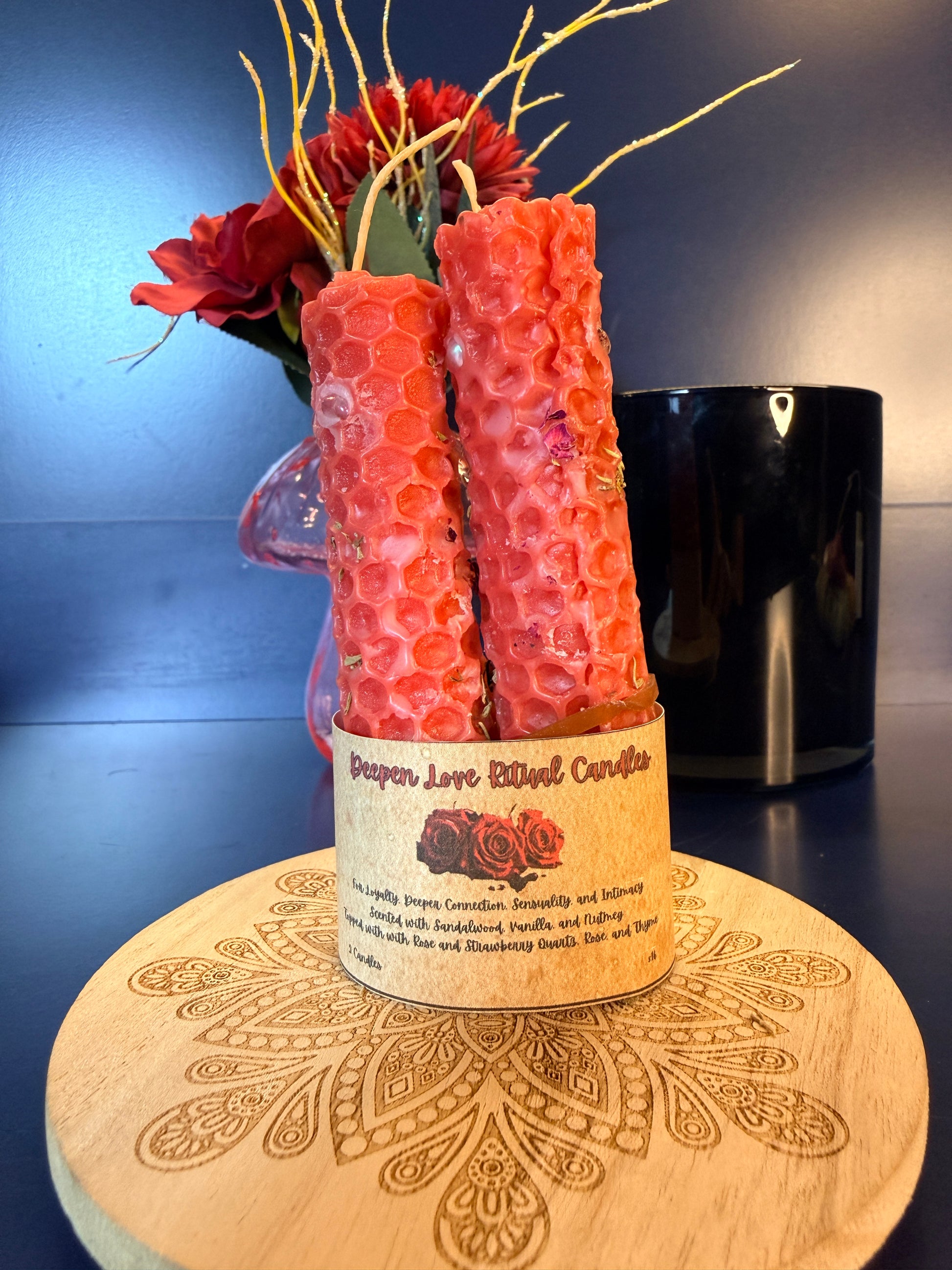 Two red candles in a decorative holder with a decorative wooden coaster and floral arrangement.