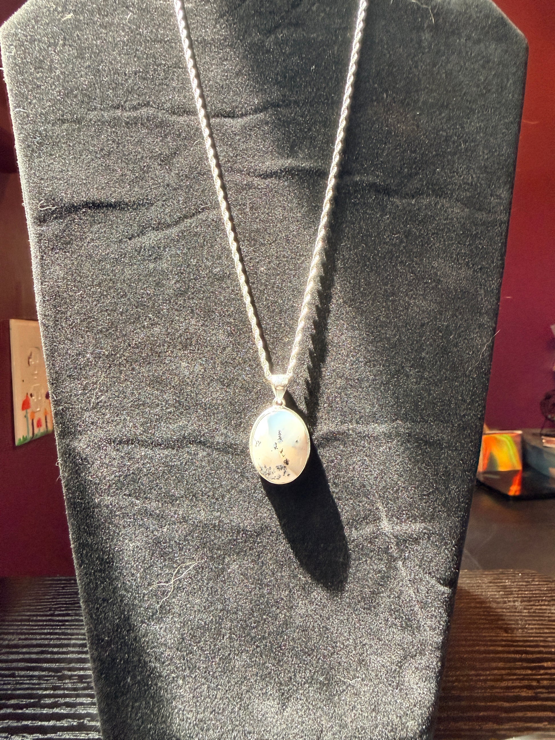 Sterling silver necklace resting on a black velvet jewelry stand holding an ovular dendrite agate pendant