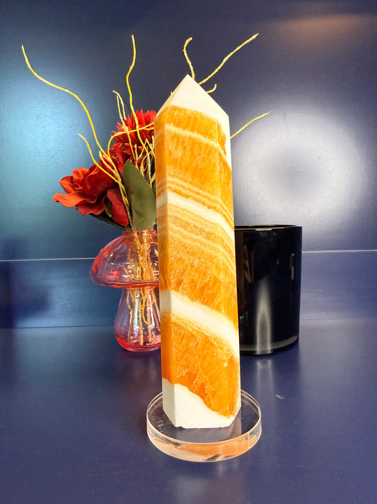 Large white and orange striped orange calcite tower in front of a red flower in a vase and black jar