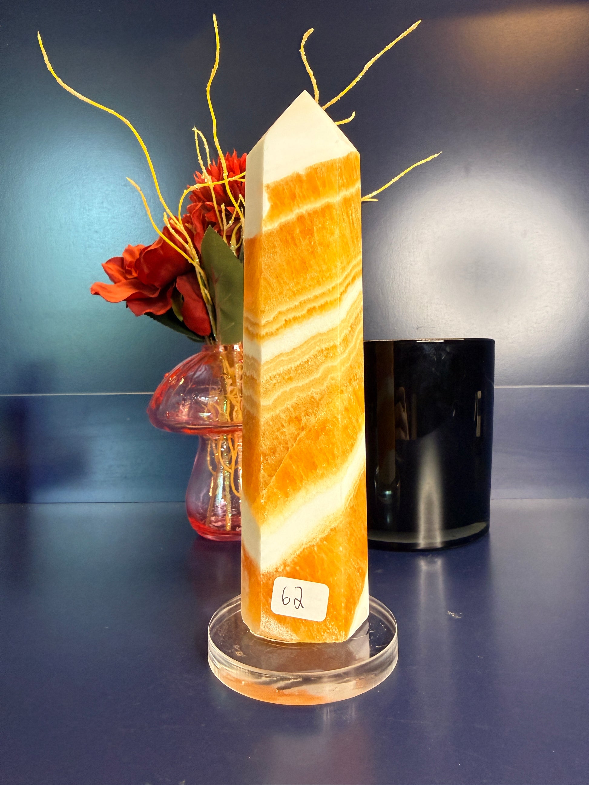 Large white and orange striped orange calcite tower in front of a red flower in a vase and black jar