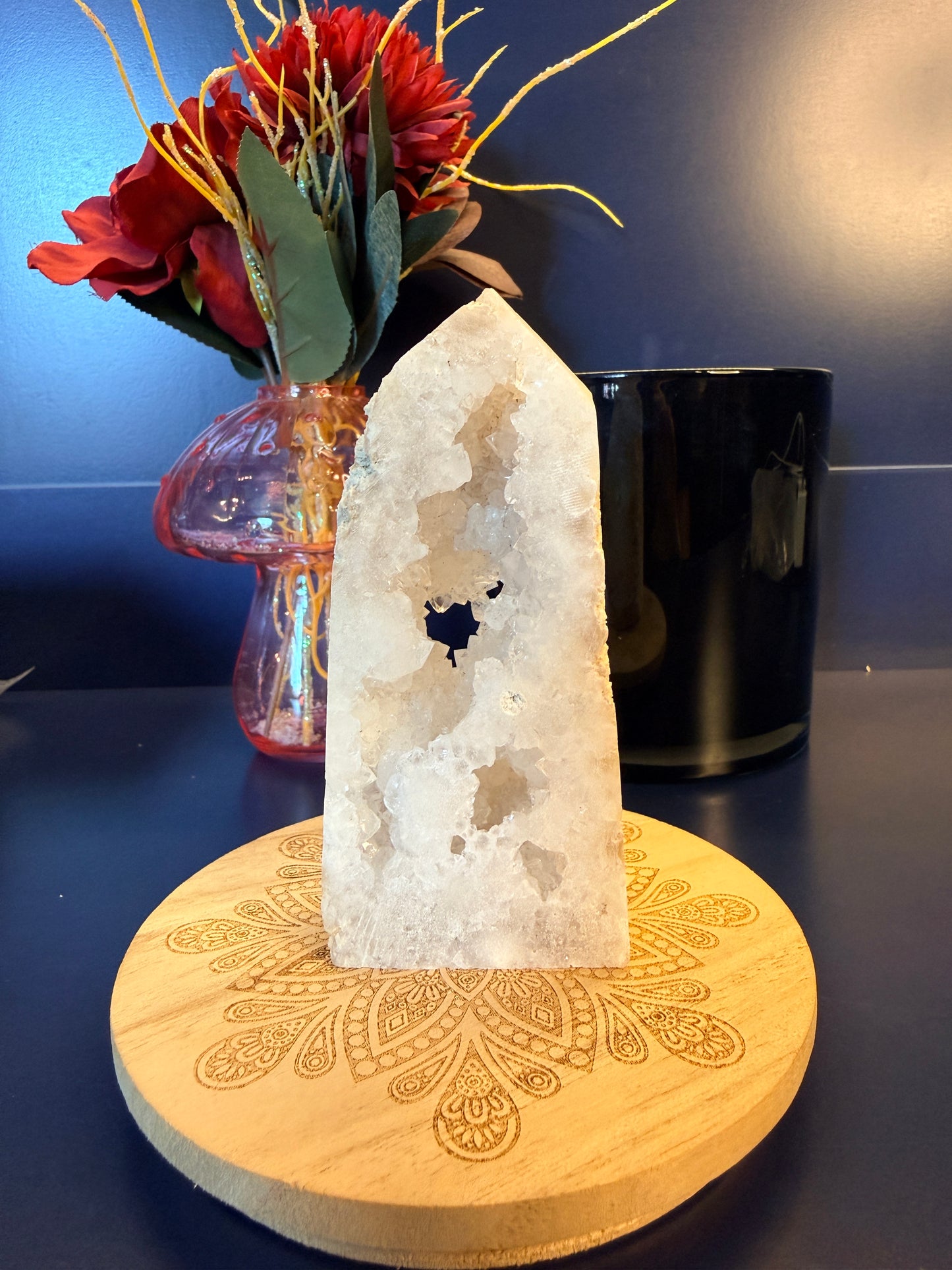 A white and sparkling crystal tower sitting on a decorative wooden coaster in front of a glass mushroom and black jar
