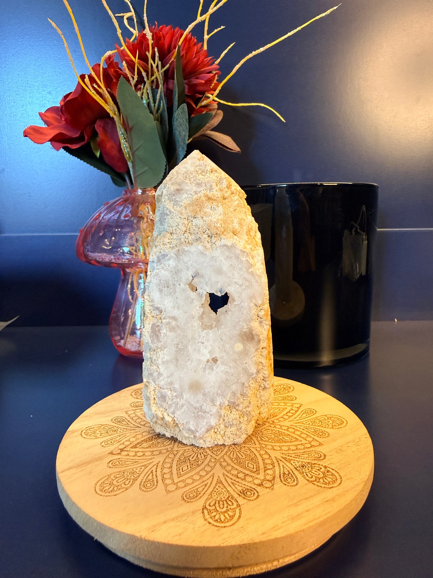 A white and sparkling crystal tower sitting on a decorative wooden coaster in front of a glass mushroom and black jar