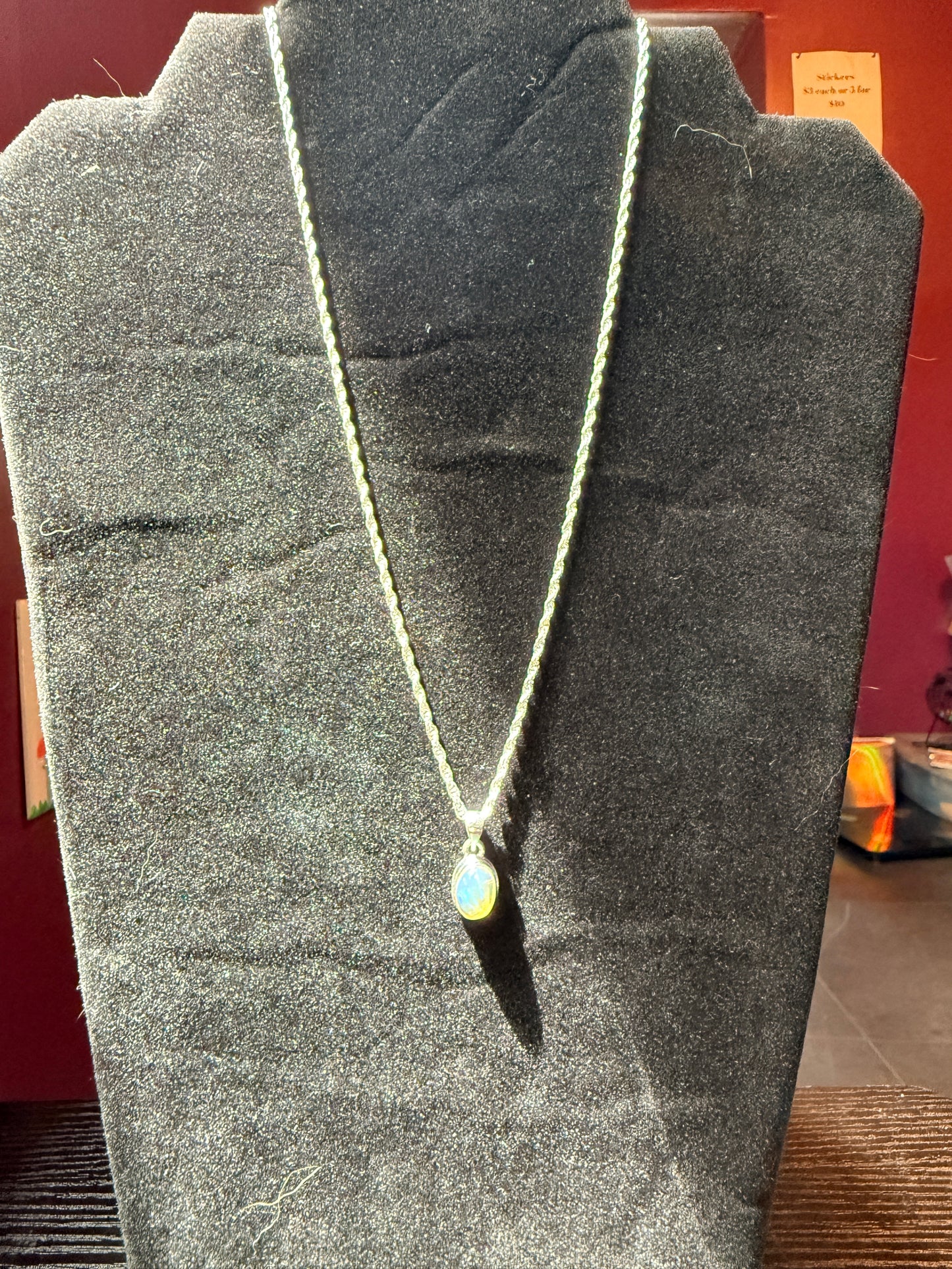 Sterling silver chain on a black velvet jewelry stand holding an ovular opal pendant