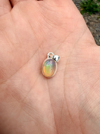 Hand holding an orange, green, and blue oval Ethiopian opal pendant