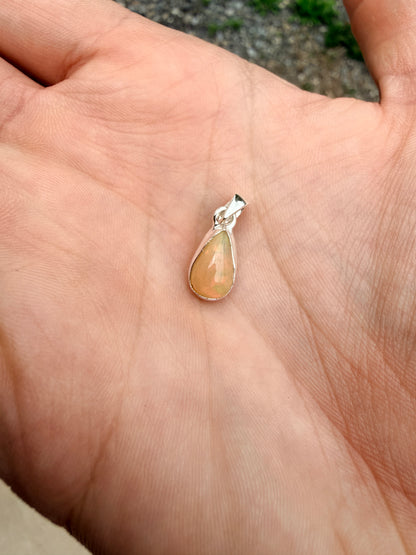 Hand holding an orange, green, and blue teardrop Ethiopian opal pendant