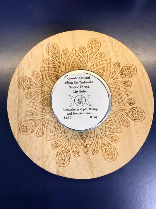 Wooden coaster with intricate patterns and a round metal lip balm on a dark blue background