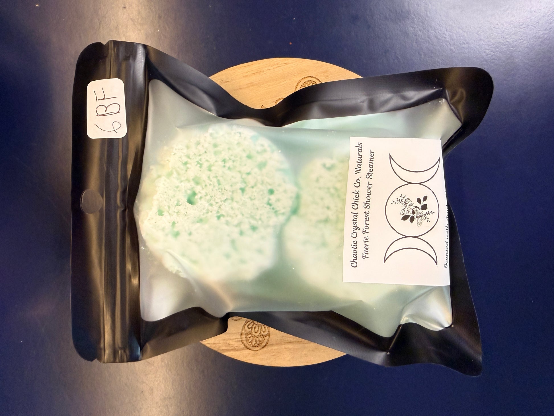 Packaged green shower steamers on a decorative wooden coaster on a blue background