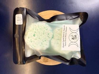 Packaged green shower steamers on a decorative wooden coaster on a blue background