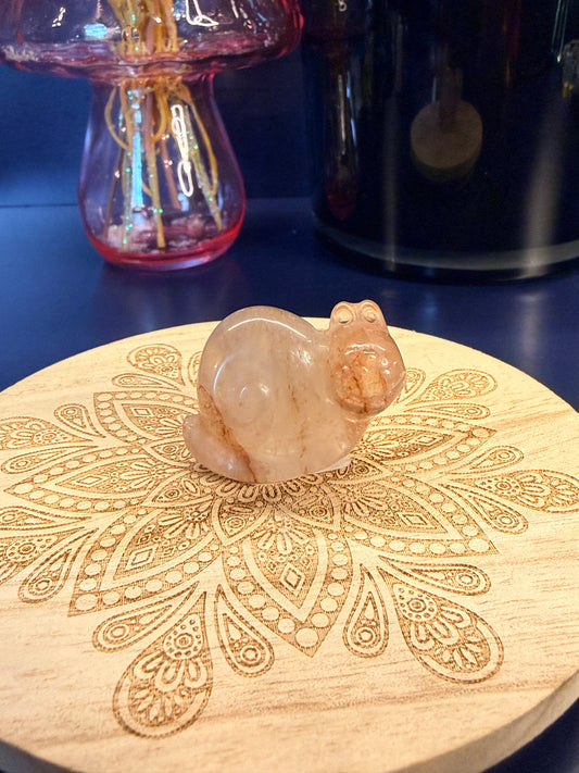 A fire quartz snail crystal sitting on a decorative wooden coaster in front of a glass mushroom and black jar