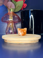 White and orange wolf head quartz carving in front of a pink vase and black jar on a wooden coaster against a blue background
