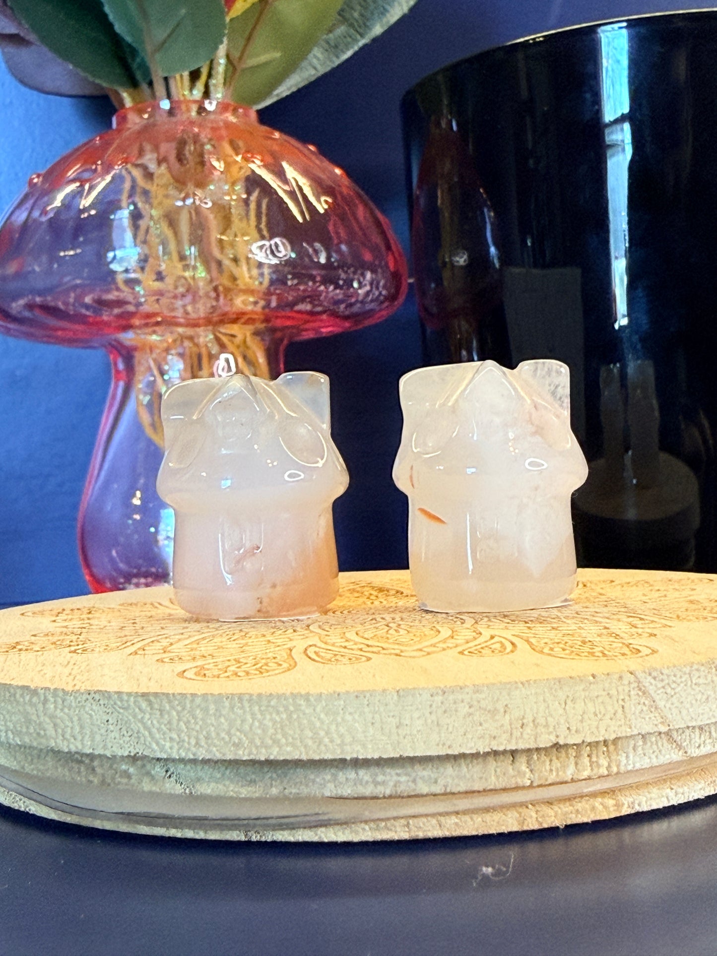 Two pale crystal houses sitting on front of a mushroom vase and black jar