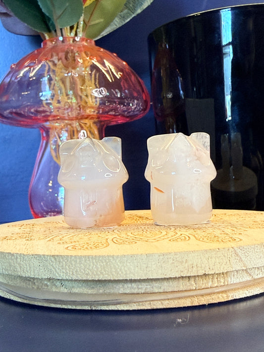 Two pale crystal houses sitting on front of a mushroom vase and black jar