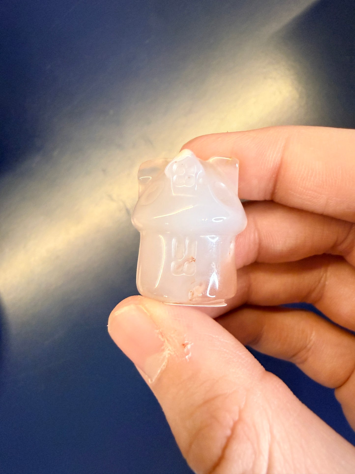 Hand holding a pale crystal house on a blue background