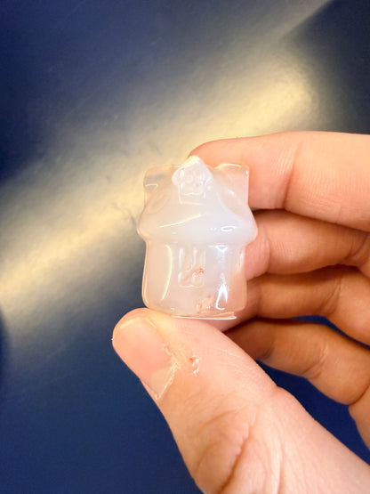 Hand holding a pale crystal house on a blue background