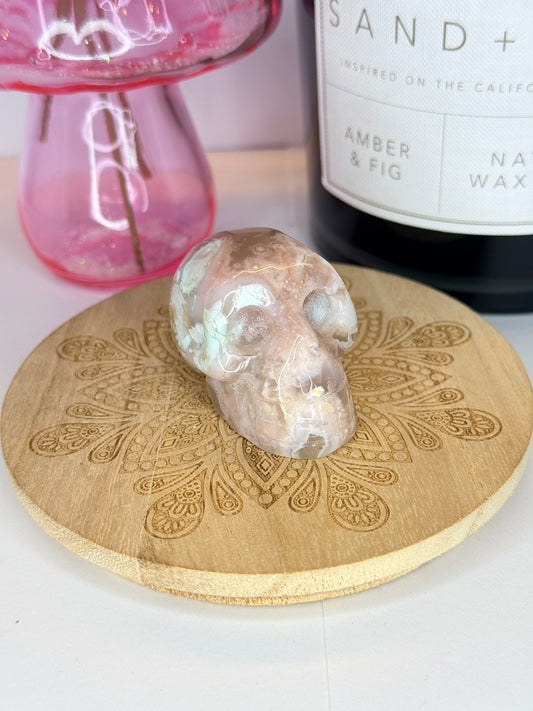 Pink and white flower agate skull on a wooden coaster in front of a black candle jar and pink vase